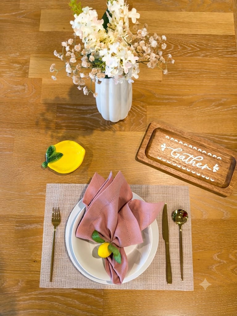 Pink Lemon table setting with woven placemat, gold flatware, and lemon napkin ring