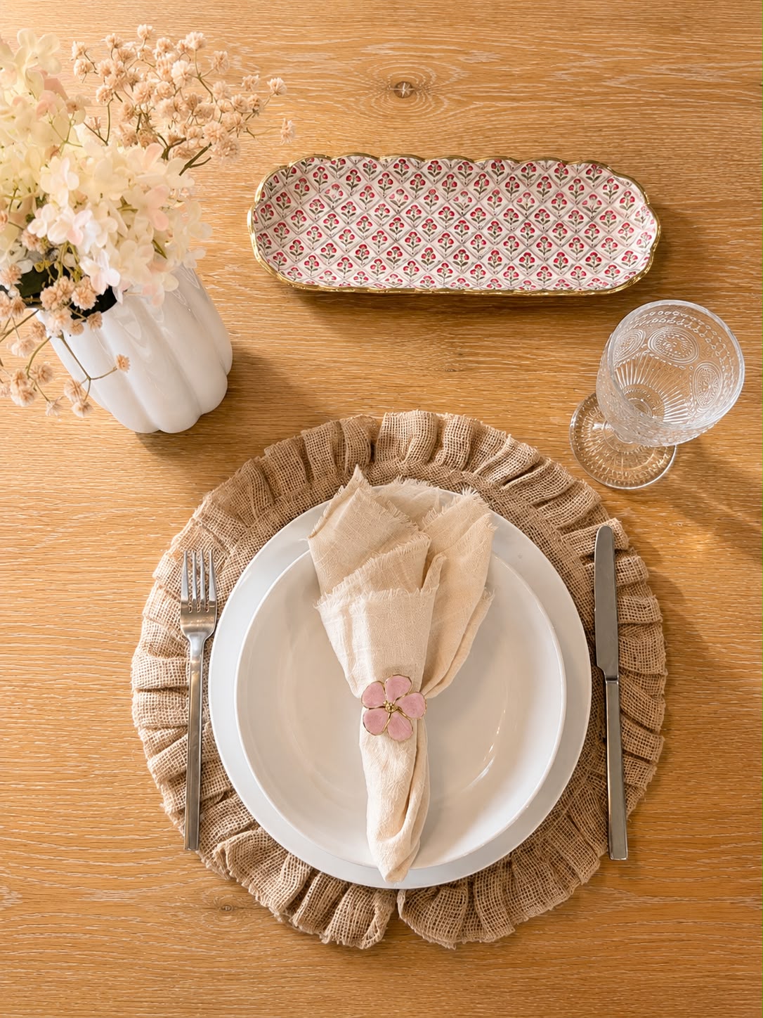 Soft Bloom table setting with ruffled jute placemat, fringed napkin, and pink metal flower napkin ring