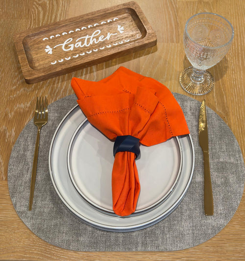 Amber Harvest table setting with grey oval placemat, orange linen napkin, and navy napkin ring